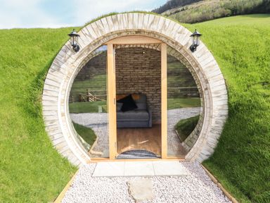 A round entrance with glass doors showing a sofa inside built into a grassy hillside at Nant y Garnedd Mallwyd near Dinas Mawddwy