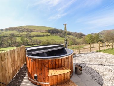 An outdoor wooden hot tub with steps and a chimney on a patio with a fence and hills in the background at Nant y Garnedd Mallwyd near Dinas Mawddwy