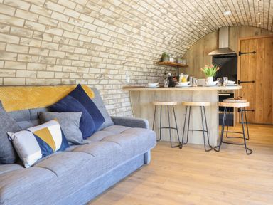 A living area with a gray sofa and pillows next to a kitchen island with wooden stools and a brick arched ceiling at Nant y Garnedd Mallwyd near Dinas Mawddwy