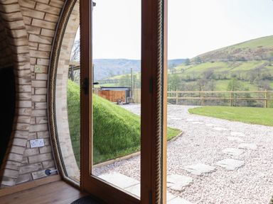 A curved wall with a glass door opening to a gravel path and grassy hill with mountains in the distance at Nant y Garnedd Mallwyd near Dinas Mawddwy