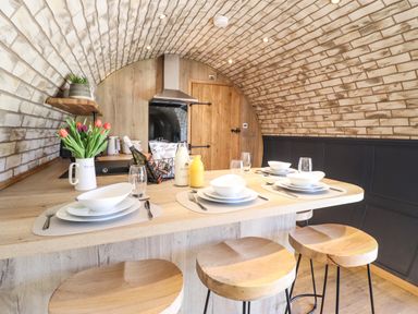 A kitchen with a wooden island set for four with bowls and glasses under a brick arched ceiling at Nant y Garnedd Mallwyd near Dinas Mawddwy