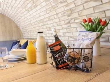 A wooden table with bottles of orange juice and milk plates a wire basket with food items and a vase with red tulips Nant y Garnedd Mallwyd near Dinas Mawddwy