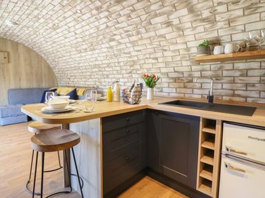 A kitchen with a wooden countertop set with dishes and glasses alongside a sitting area with a blue sofa at Nant y Garnedd Mallwyd near Dinas Mawddwy