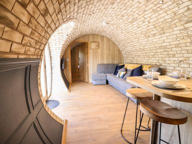 A living area with a curved brick ceiling a gray sofa with cushions a wooden dining table set with dishes and stools and a wooden floor at Nant y Garnedd Mallwyd near Dinas Mawddwy