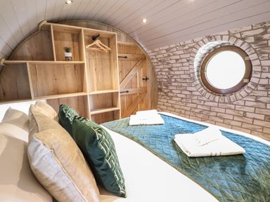 A bedroom with a bed with pillows and towels near a wooden shelf unit and a round window at Nant y Garnedd Mallwyd near Dinas Mawddwy