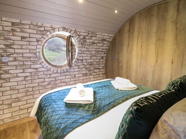 A bedroom with a round window a bed with blue bedding and folded towels on the bed at Nant y Garnedd Mallwyd near Dinas Mawddwy