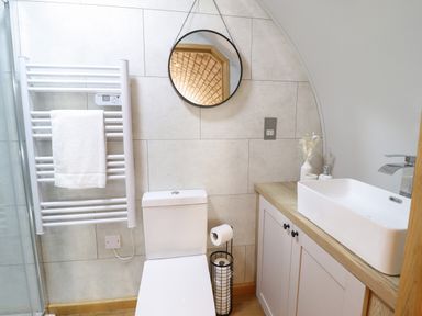 A bathroom with a white toilet a heated towel rail with a towel a round mirror and a sink on a wooden countertop at Nant y Garnedd Mallwyd near Dinas Mawddwy