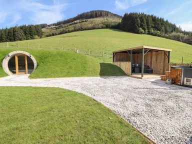An outdoor area with a grass-covered round door entrance a gravel pathway wooden gazebo with seating and a hot tub on a patio Nant y Garnedd Mallwyd near Dinas Mawddwy