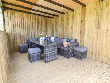 A covered outdoor seating area with wicker furniture and a glass table at Nant y Garnedd in Mallwyd near Dinas Mawddwy