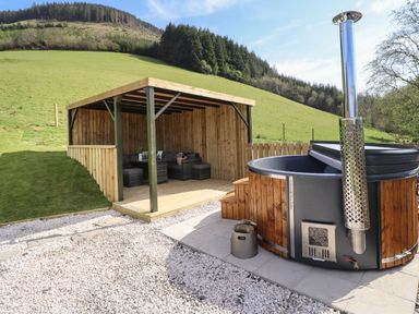 An outdoor wooden gazebo with seating and a hot tub on a paved area in a grassy hillside at Nant y Garnedd Mallwyd near Dinas Mawddwy