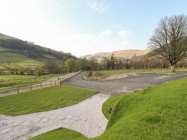 A gravel driveway and grass lawn with wooden fences and hills in the background at Nant y Garnedd Mallwyd near Dinas Mawddwy