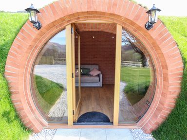 A circular entrance with glass doors leading to a room with a sofa and two cushions at Nant yr Esgair in Mallwyd near Dinas Mawddwy
