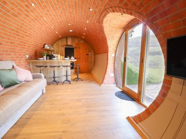 An arched brick interior with a kitchen island and stools a sofa and glass doors opening to outside at Nant yr Esgair Mallwyd near Dinas Mawddwy