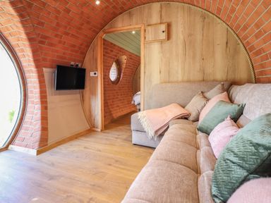 A living space with curved brick walls a wooden door a mounted flat screen tv and a beige sofa with pillows and a throw at Nant yr Esgair Mallwyd near Dinas Mawddwy