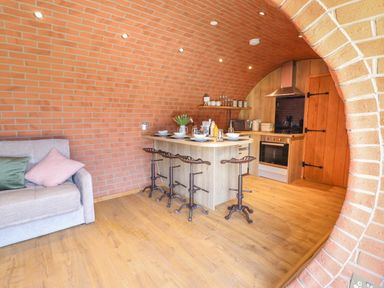 A kitchen with a wooden island counter and metal stools next to a gray sofa in a brick vaulted room at Nant yr Esgair Mallwyd near Dinas Mawddwy