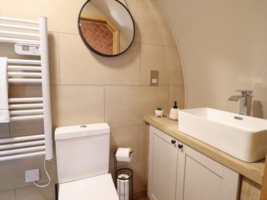 A bathroom with a toilet a sink with cabinet a round mirror a heated towel rail and a toilet paper holder at Nant yr Esgair in Mallwyd near Dinas Mawddwy