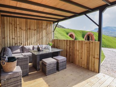 An outdoor covered patio with wicker furniture and a table with glasses and flowers at Nant yr Esgair Mallwyd near Dinas Mawddwy