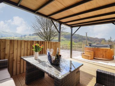 An outdoor covered seating area with a glass table holding a vase of flowers and wine at Nant yr Esgair Mallwyd near Dinas Mawddwy