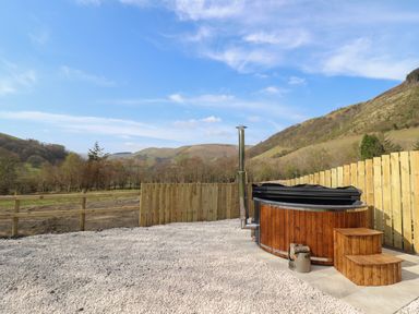 An outdoor hot tub with wooden steps and a fence surrounding a gravel area with hills in the background at Nant yr Esgair Mallwyd near Dinas Mawddwy