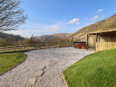An outdoor area with gravel path, wooden hot tub, wooden shelter, grassy slopes, and hills in the background at Nant yr Esgair Mallwyd near Dinas Mawddwy