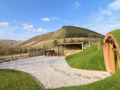 An outdoor area with a wooden hot tub and covered structure next to grass-covered earth buildings at Nant yr Esgair Mallwyd near Dinas Mawddwy