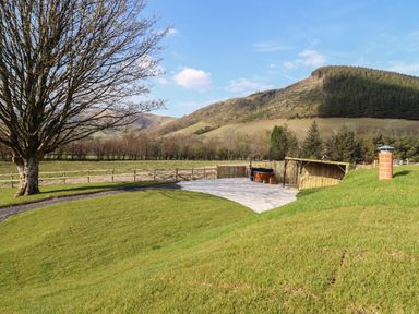 A grassy outdoor area with a tree a fenced field a small wooden shelter and hills in the background at Nant yr Esgair Mallwyd near Dinas Mawddwy