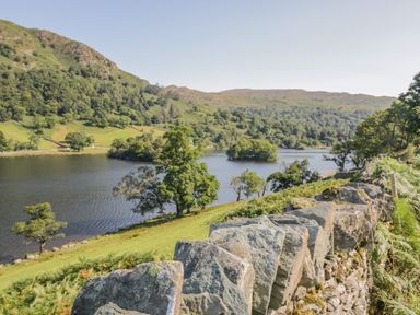 A lake surrounded by hills and trees with a stone wall in the foreground at Kirkstone Lodge in Limefitt Park near Windermere