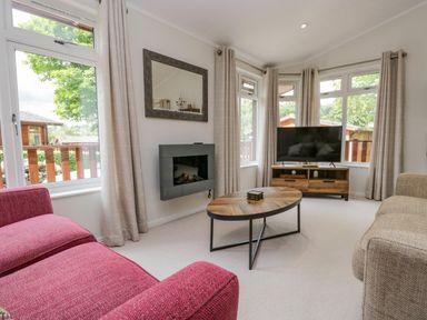 A living room with a red sofa a beige sofa wooden coffee table a wall-mounted fireplace and a television on a wooden stand at Kirkstone Lodge in Limefitt Park near Windermere