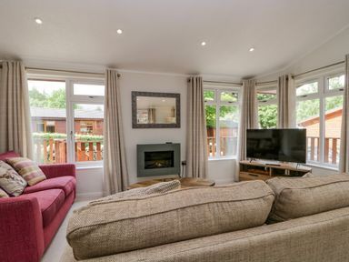 A living room with a beige sofa a red armchair a TV on a wooden stand and windows with curtains at Kirkstone Lodge Limefitt Park near Windermere