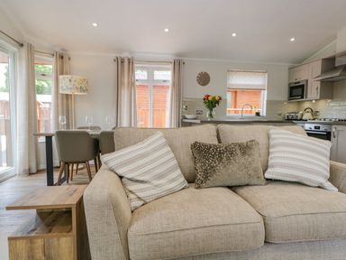 A living room with a beige sofa and pillows a dining table with chairs and a kitchen area with appliances at Kirkstone Lodge in Limefitt Park near Windermere