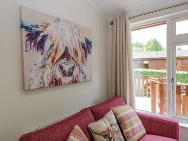 A red sofa with patterned cushions and a painting of a highland cow above it in a living room at Kirkstone Lodge in Limefitt Park near Windermere