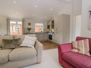 An open living room and kitchen area with beige and red sofas with cushions at Kirkstone Lodge in Limefitt Park near Windermere