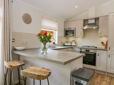 A kitchen with a countertop island with two wooden stools flowers on the counter and built-in oven at Kirkstone Lodge in Limefitt Park near Windermere