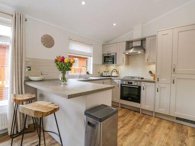 A kitchen with two wooden stools flowers on the countertop and modern appliances at Kirkstone Lodge in Limefitt Park near Windermere