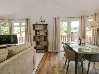 A living room and dining area with a sofa, shelving unit, dining table, chairs, and glass doors at Kirkstone Lodge in Limefitt Park near Windermere