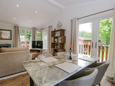 A dining table with wine glasses and placemats next to a living area with a sofa a TV and shelving at Kirkstone Lodge in Limefitt Park near Windermere