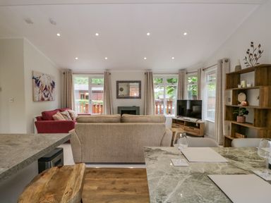 A living room with a beige sofa a red sofa a television on a wooden stand a wooden shelving unit and a marble dining table at Kirkstone Lodge in Limefitt Park near Windermere
