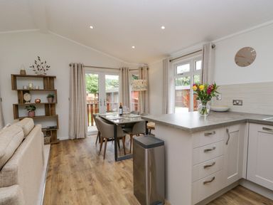A dining area with a table and chairs next to a kitchen countertop with a vase of flowers at Kirkstone Lodge in Limefitt Park near Windermere