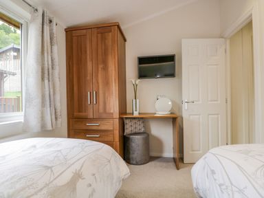 A bedroom with two beds a wooden wardrobe a wall-mounted television and a desk with a vase and lamp at Kirkstone Lodge Limefitt Park near Windermere