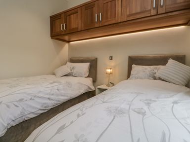 A bedroom with two single beds and wooden cabinets above at Kirkstone Lodge in Limefitt Park near Windermere