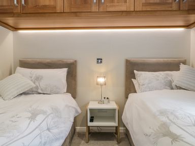 A bedroom with two single beds a nightstand with a lamp and remote between them at Kirkstone Lodge in Limefitt Park near Windermere