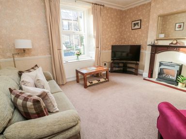 A living room with a green sofa, wooden coffee table, television, fireplace, and window at 19 Duke Street in Alnwick