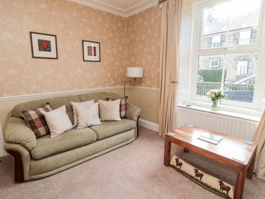 A sitting room with a green sofa and cushions a wooden coffee table and a window with flowers on the sill at 19 Duke Street in Alnwick