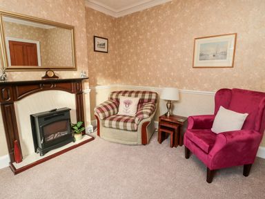 A sitting room with a plaid armchair a red armchair a wooden fireplace and a floor lamp at 19 Duke Street in Alnwick