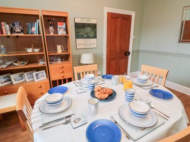 A dining room with a round table set with blue and white dishes croissants in the middle and wooden chairs at 19 Duke Street in Alnwick