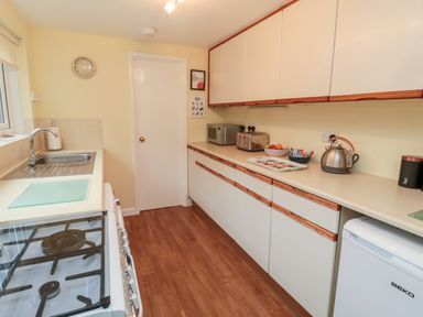 A kitchen with a gas stove, sink, countertop appliances, white cabinets, and wooden floor at 19 Duke Street in Alnwick