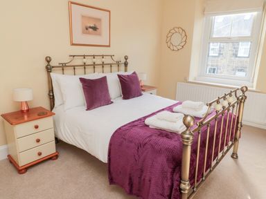 A bedroom with a metal bed frame purple pillows and throw near a window at 19 Duke Street in Alnwick