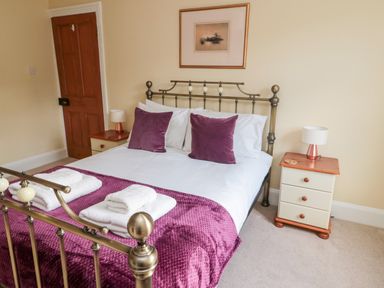A bedroom with a metal bed frame purple pillows and blanket two bedside tables with lamps and a wooden door at 19 Duke Street in Alnwick