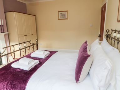 A bedroom with a bed made with white linens and purple pillows and a purple throw at 19 Duke Street in Alnwick