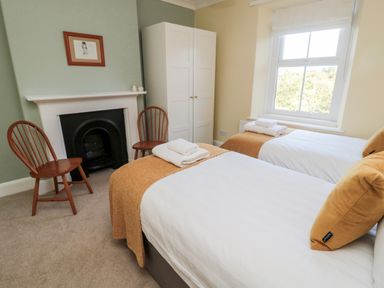 A bedroom with two single beds with white linens and brown throws by a window and a fireplace with two wooden chairs 19 Duke Street in Alnwick